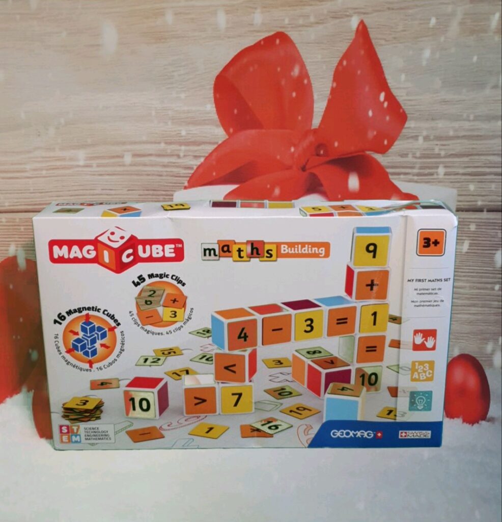 A box of Magicube Maths Building blocks for ages 3+, featuring colourful magnetic cubes with numbers and symbols, displayed against a festive background with a large red bow and ornaments—one of the must-have gifts for children Christmas 2020.