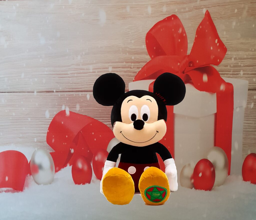 A plush Mickey Mouse toy sits in front of a festive background with red and white wrapped gift boxes, red baubles, and snow—one of the must-have gifts for children Christmas 2020.