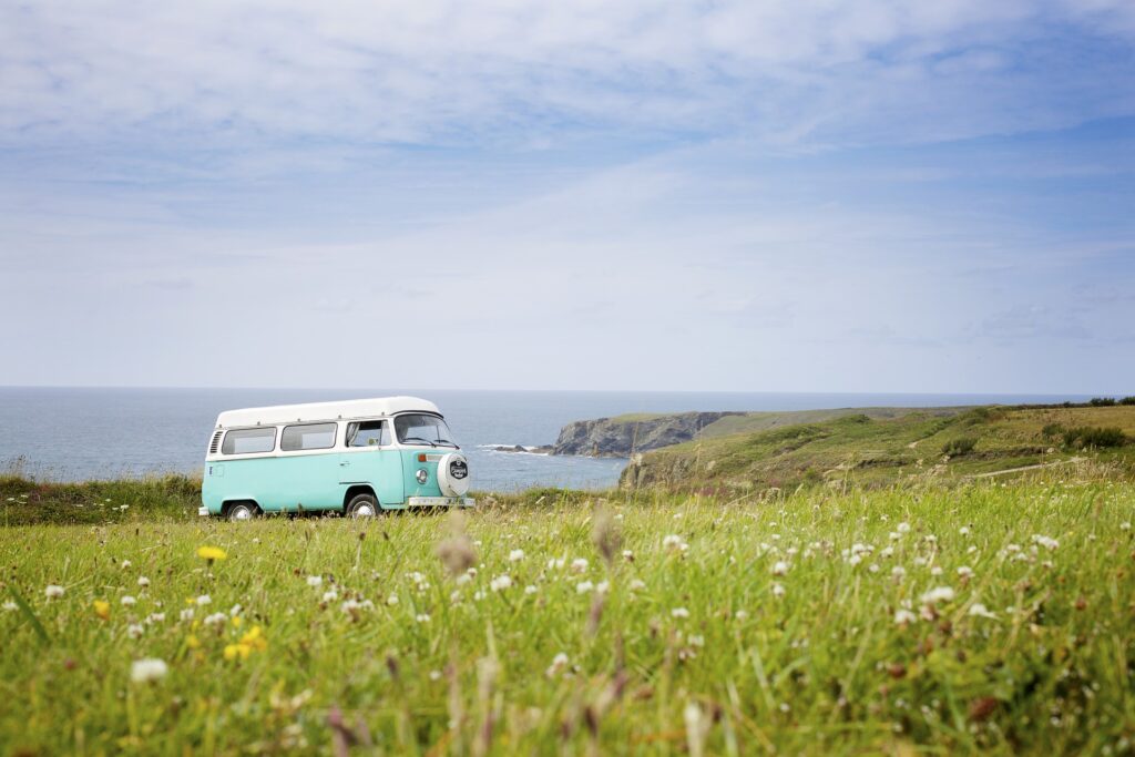 A blue and white campervan parked up on a cliff overlooking the sea