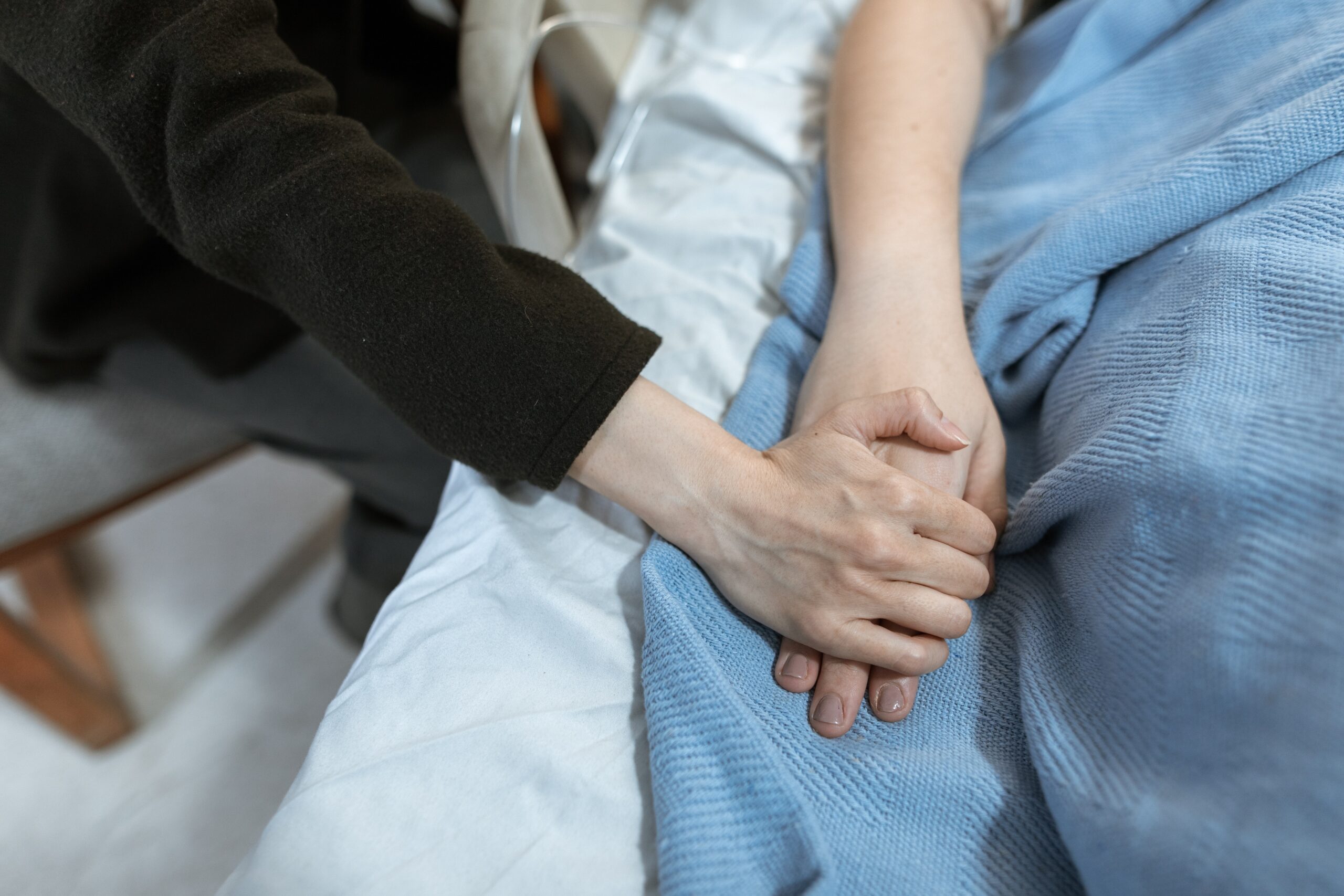 someone in a hospital bed having their hand held by their partner