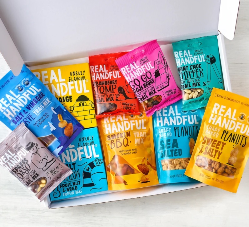 A box containing eight colourful packets of Real Handful snacks, ideal as Father’s Day gifts, featuring flavours like orange, strawberry, BBQ, mint choc, blueberry, and sweet & salty—all arranged neatly on a white surface.