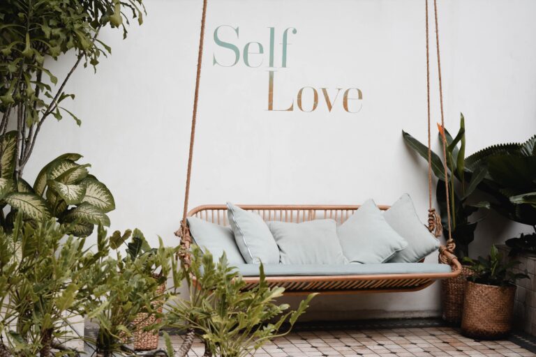 a bench hanging in a garden with self love written on a white wall behind