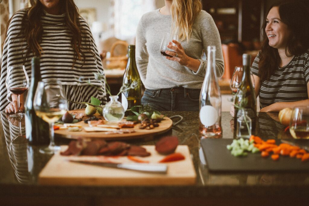Three women gather around a kitchen island with wine and snacks, chatting and enjoying each other's company—a perfect example of why a serviced flat is perfect for entertaining guests in a cosy indoor setting.