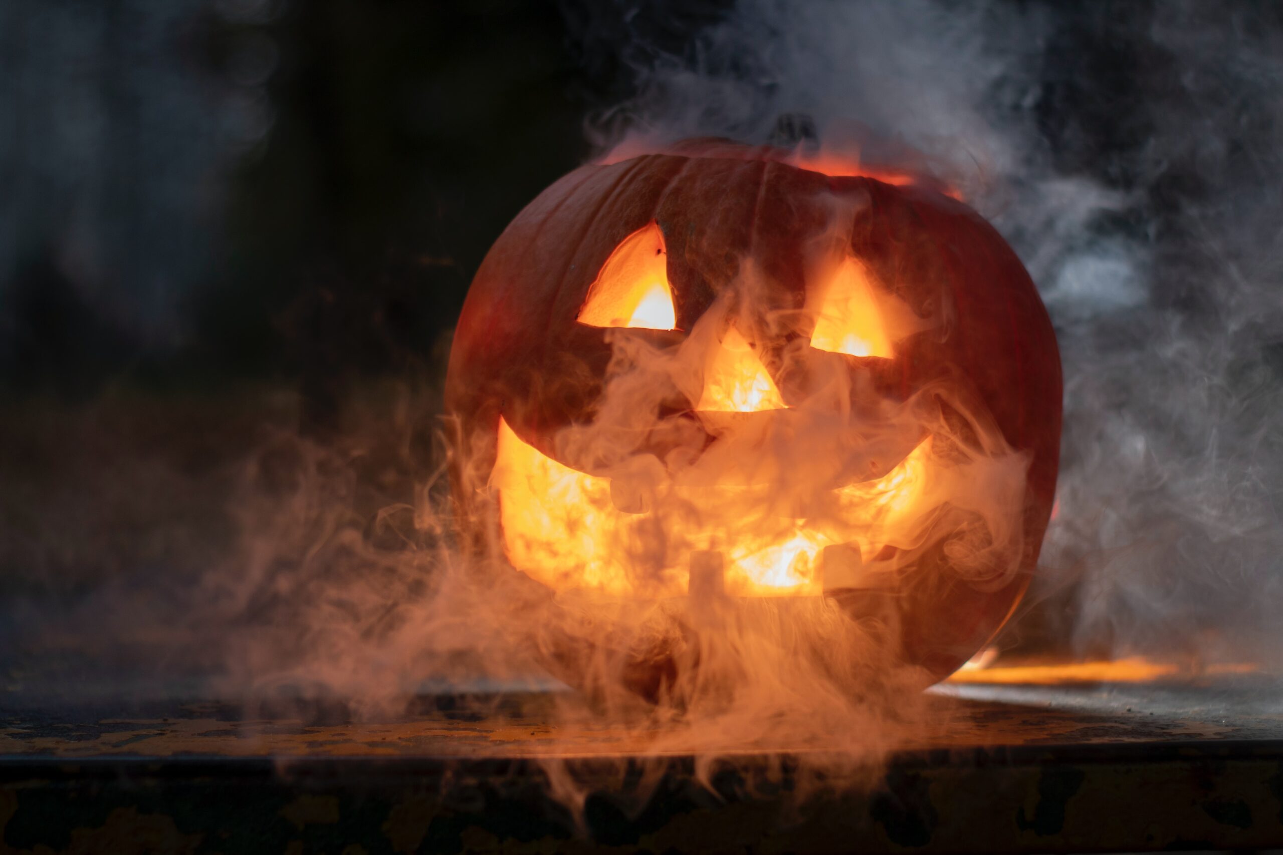 A glowing jack-o’-lantern with a carved smiling face sits on a surface, surrounded by swirling smoke in the dark, capturing the spooky spirit of Hallowe’en 2021.