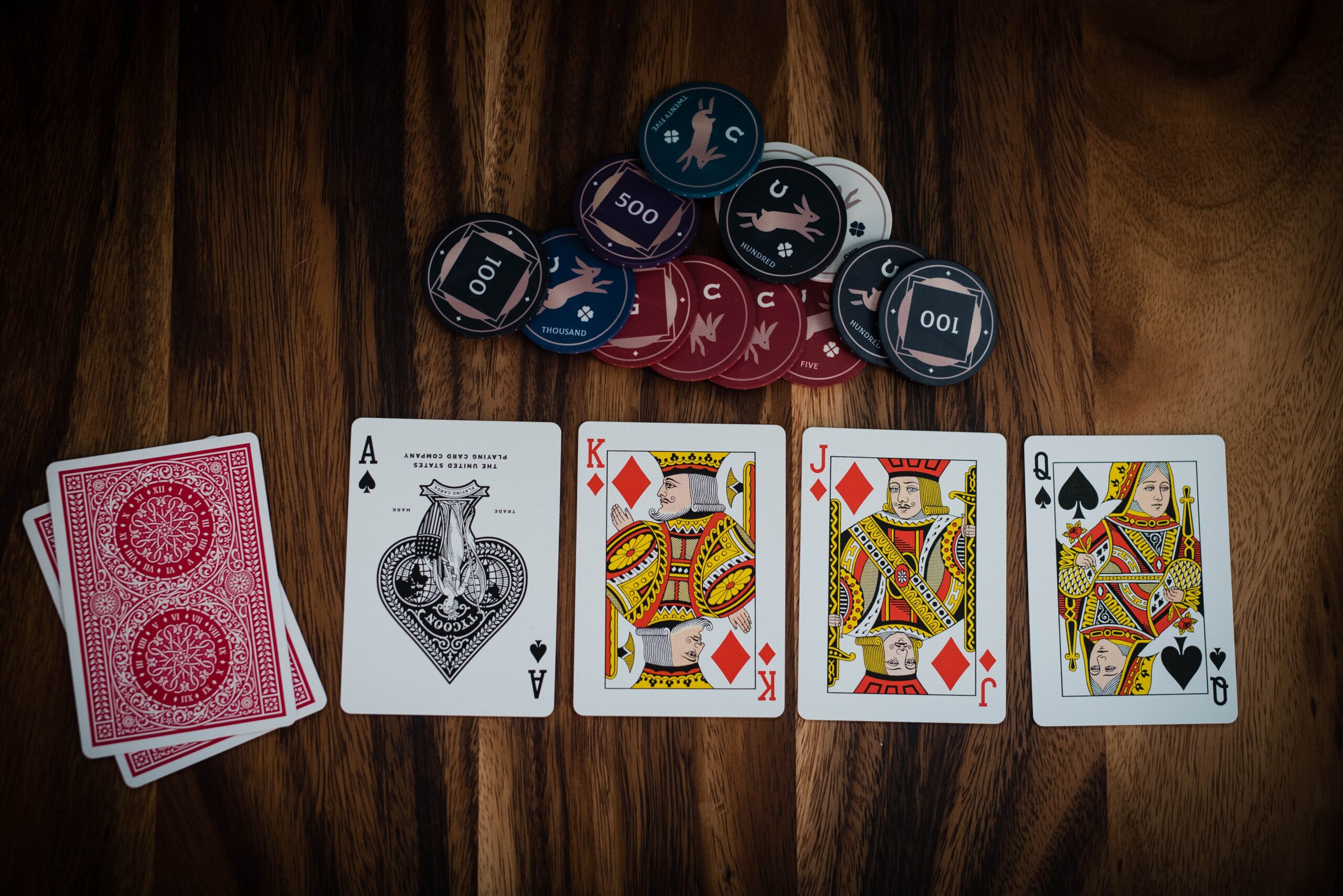 Four playing cards—Ace of Spades, King of Hearts, Jack of Diamonds, and Queen of Spades—are laid out on a wooden table with poker chips and a face-down pack, capturing the thrill echoed by the increasing demand for online casinos.