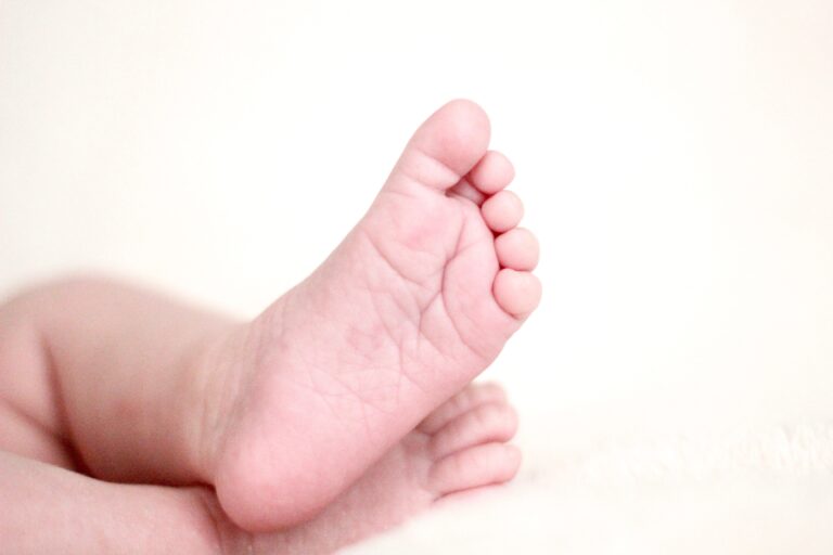 Close-up of a baby’s feet resting on a soft, white surface, with toes slightly curled—a sweet reminder in "First Time for Everything: When to Do What with Your Child." The background is gently out of focus.