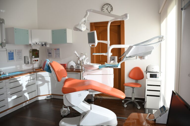 Bright dental surgery with an orange dentist's chair, overhead light, dental equipment, cupboards, a clock on the wall, and sunlight streaming in—everything you need for What to Know About Your Next Dental Appointment.