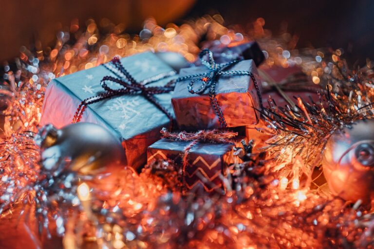 A group of wrapped presents with decorative ribbons sits among shiny tinsel, glowing fairy lights, and metallic baubles—perfect gift ideas for adults Christmas 2021, creating a festive holiday atmosphere.