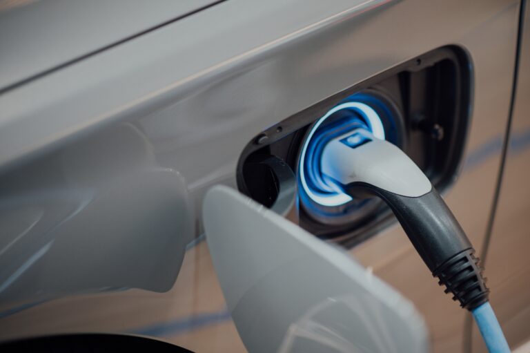 A close-up of an electric vehicle being charged, showing a charging plug connected to the car’s charging port and a blue light glowing around it—demonstrating how you can align with the Cop26 message by choosing cleaner transport.