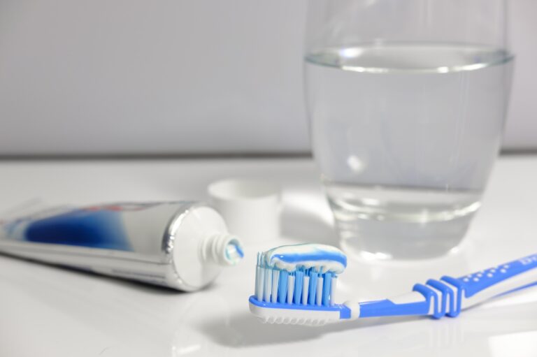 a toothbrush with toothpaste on the bristles, sat next to a tube of opened toothpaste and a glass of water