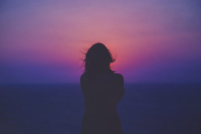 Silhouette of a person with loose hair standing against a vibrant sunset sky, reflecting on 5 Tips for Dealing With Toxic People in Your Life as shades of purple, pink, and blue blend on the horizon.