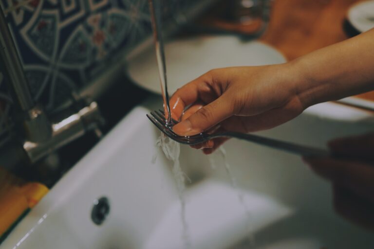 A person washing cutlery in the sink under a running tap