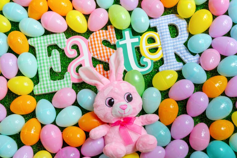 Colourful plastic Easter eggs surround a plush pink bunny and large decorative letters spelling "Easter" on a green background, offering fun Easter gift ideas for children.