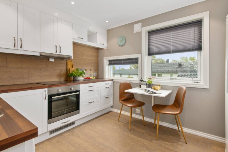 Modern kitchen with white cupboards, built-in oven, wooden worktops, and tan tiled floors—perfect inspiration if you're looking for ways to update your tired-looking kitchen. A small table by the window creates a cosy dining spot.