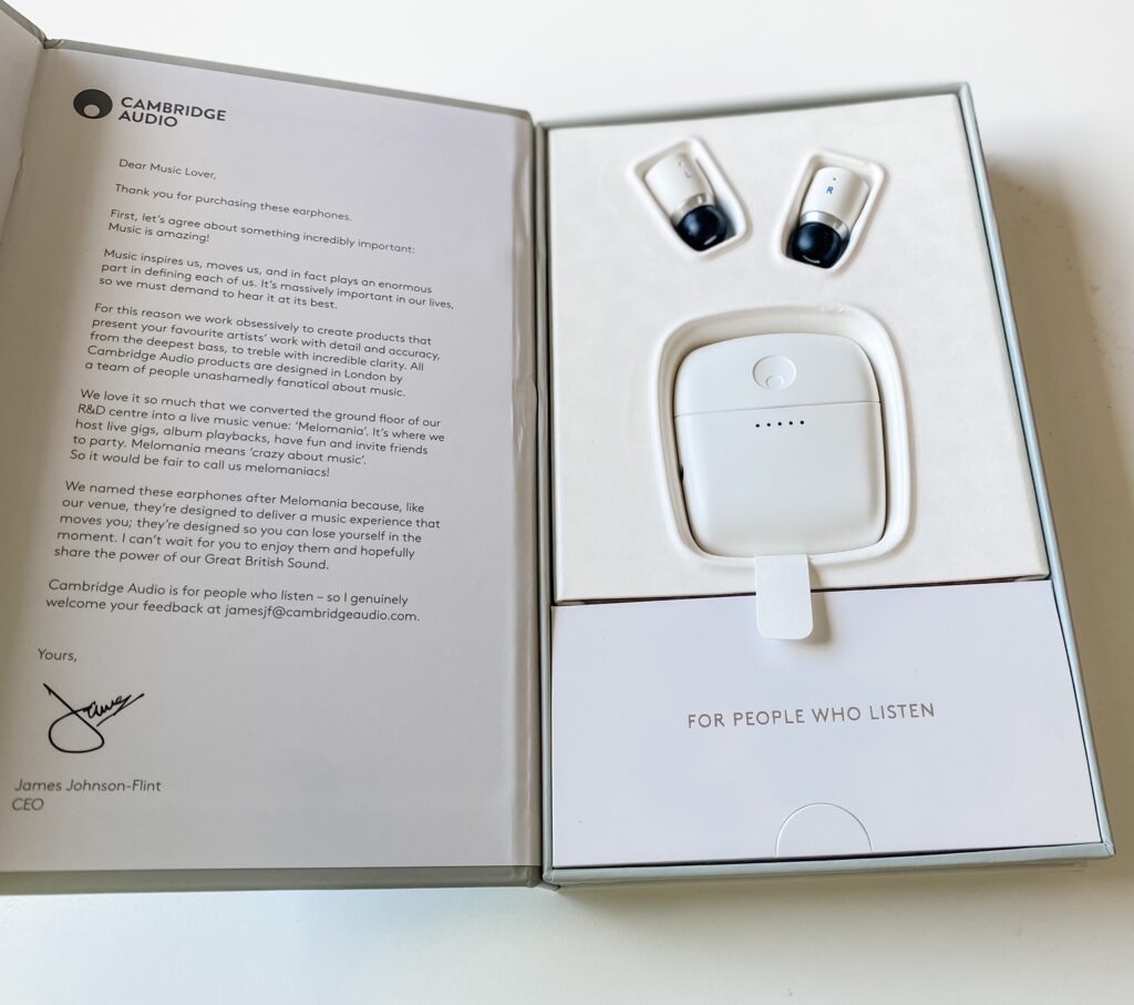 Open box displaying Cambridge Audio earbuds and charging case on the right, and a printed welcome letter from the CEO on the left, addressed to music lovers as part of a Summer Prize Giveaway from Top UK Bloggers, emphasising the importance of sound quality.
