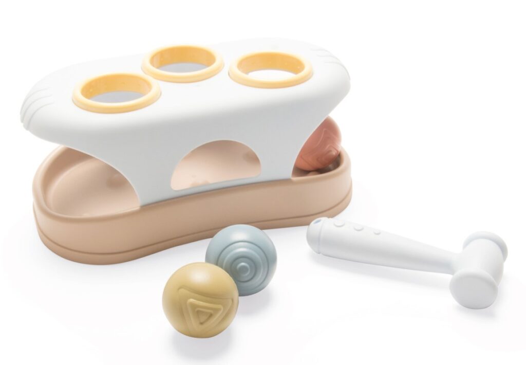 A plastic toy with three coloured balls, a white hammer, and a base with three holes for the balls to be hammered through—perfect for Toys and Games to Keep The Kids Busy. The toy is beige, white, and yellow, set against a white background.