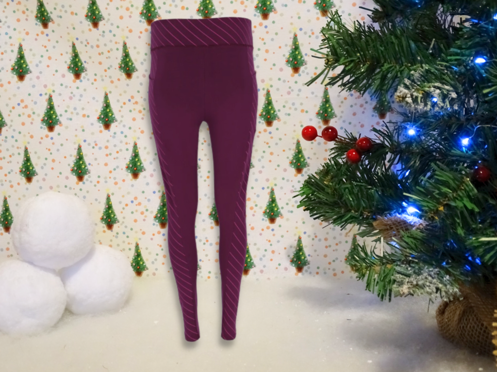 A pair of purple leggings with diagonal stripes displayed in front of a festive holiday-themed background—perfect for snow, snowballs, and small Christmas trees. These leggings make stylish gift ideas for adults 2022.