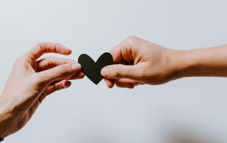Two hands holding a small black paper heart together against a plain white background evoke connection, love, or support—much like the comfort offered by helplines in times of need.