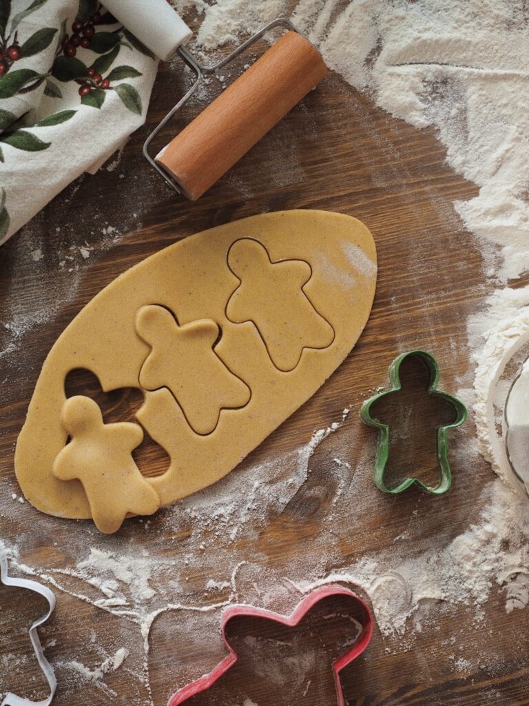 Gingerbread dough on a floured wooden surface with three gingerbread men shapes cut out, surrounded by biscuit cutters and a rolling pin—baking could be one of the 5 New Hobbies to Take Up in 2023.