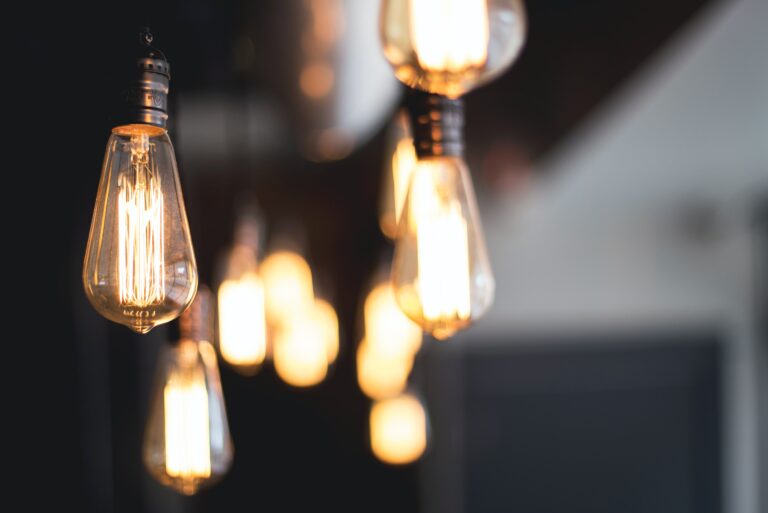 A row of vintage-style Edison light bulbs hangs from the ceiling, glowing warmly against a dark background—a stylish choice that can help your household to save money during the cost-of-living crisis by using energy-efficient lighting.
