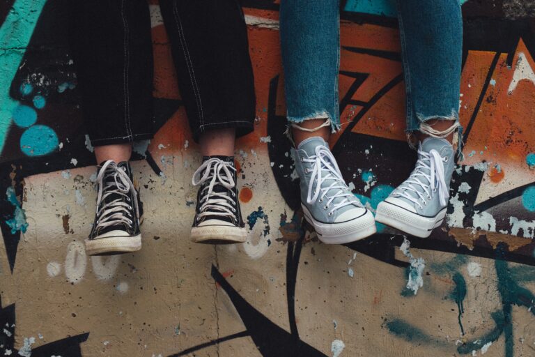 Two people sit side by side, legs dangling and sporting trendy high-top trainers and frayed jeans, against a vibrant graffiti wall—perfect inspiration for the 10 Engaging Activities for Teenagers looking to add colour to their days.