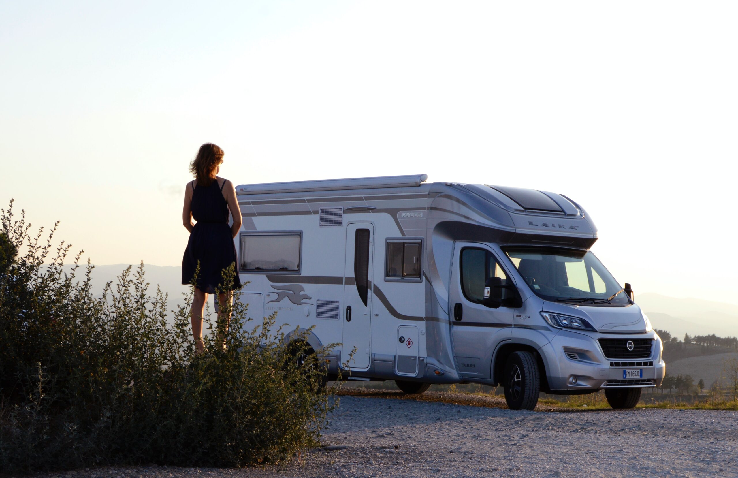 A woman stood next to a white motorhome at sunset