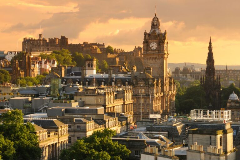 A cityscape of Edinburgh at sunset, featuring the historic Edinburgh Castle on a hill and the Balmoral Hotel clock tower, bathed in golden light—a stunning view of a city renowned for its vibrant festivals.