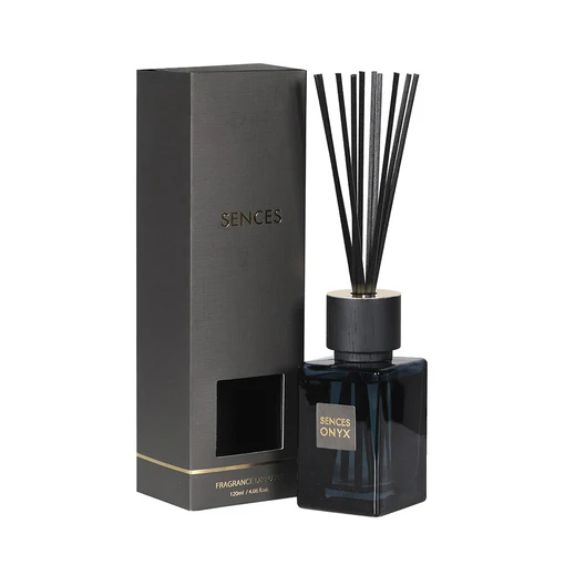 A black reed diffuser bottle labelled "SENCES ONYX" with black reeds, placed next to its matching black and gold packaging box labelled "SENCES," adds a touch of elegance whilst infusing your space with a luxurious aroma.