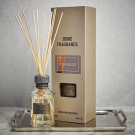 A glass reed diffuser labelled "Ocean Breeze" fills the air with a fresh aroma as it rests on a silver tray beside a tall beige box labelled "Home Fragrance," both featuring matching branding.