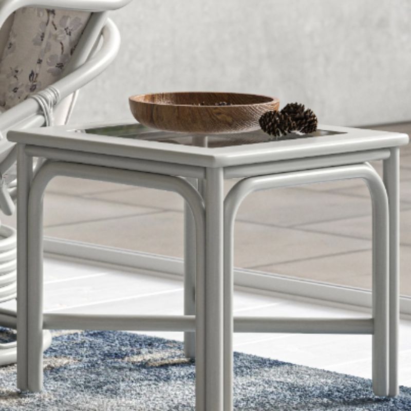 A small white side table with a glass top, holding a wooden bowl and two pine cones, adds unique style to the room. Part of a chair and a patterned rug are visible nearby.