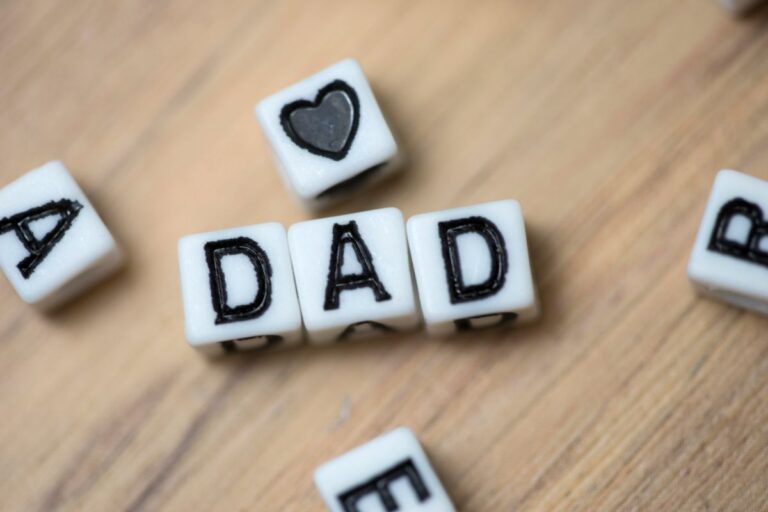 White lettered cubes on a wooden surface spell out "DAD," with a cube featuring a black heart symbol nearby—much like cherished private number plates, these cubes create a personalised and meaningful scene. Other scattered cubes are partially visible at the edges.