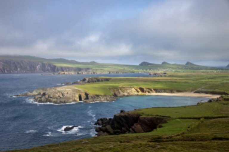 A blurred image of an Aran coastal landscape featuring rocky cliffs, grassy fields, and a calm sea under a cloudy sky.