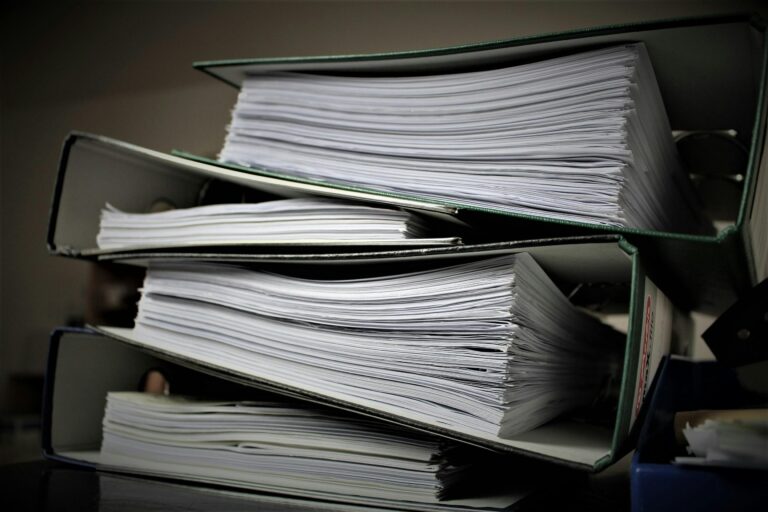 Three large folders filled with stacks of paper are piled horizontally, capturing the overwhelming nature of life admin and extensive documentation.