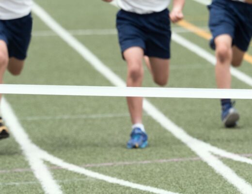 Three children in sports kit dash towards a finishing line on a track during sports day, their legs pounding the ground as they near the tape.