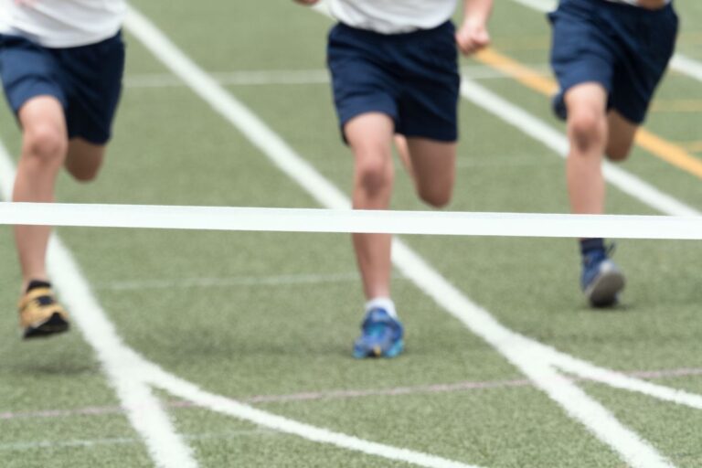 Three children in sports kit dash towards a finishing line on a track during sports day, their legs pounding the ground as they near the tape.