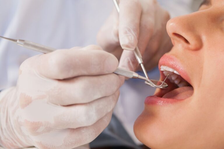 A dentist wearing gloves uses dental instruments to examine a patient's open mouth during a dental check-up, ensuring their dental hygiene routine is effective.
