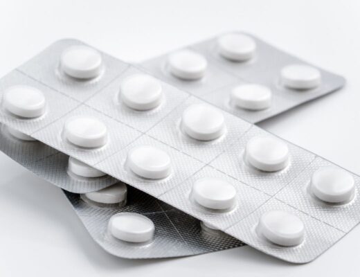 Three blister packs of round white tablets arranged in a staggered stack on a white surface. Each pack contains several pills, with some tablets visible through the clear packaging.