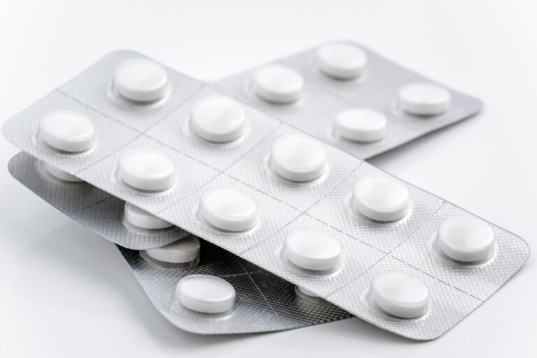 Three blister packs of round white tablets arranged in a staggered stack on a white surface. Each pack contains several pills, with some tablets visible through the clear packaging.