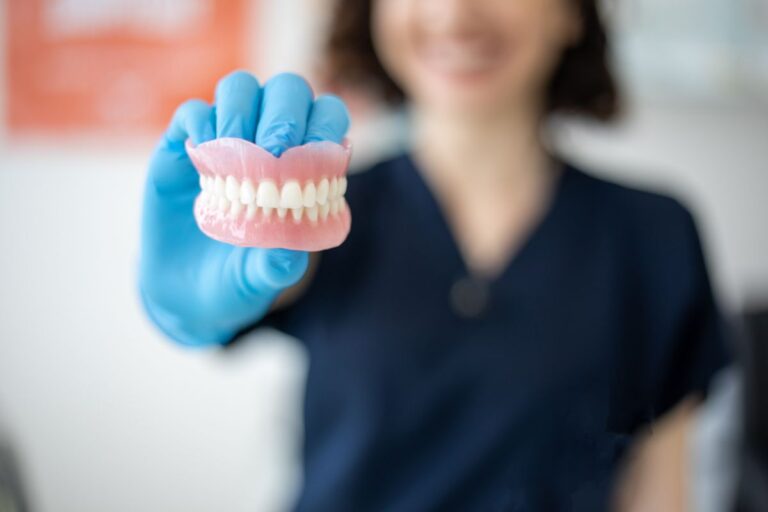 A dental professional wearing blue gloves holds a set of natural, high-quality dentures.